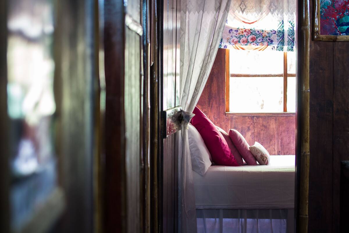 Ein Zimmer mit Bett, einem Vorhangfenster und Blick nach draußen.