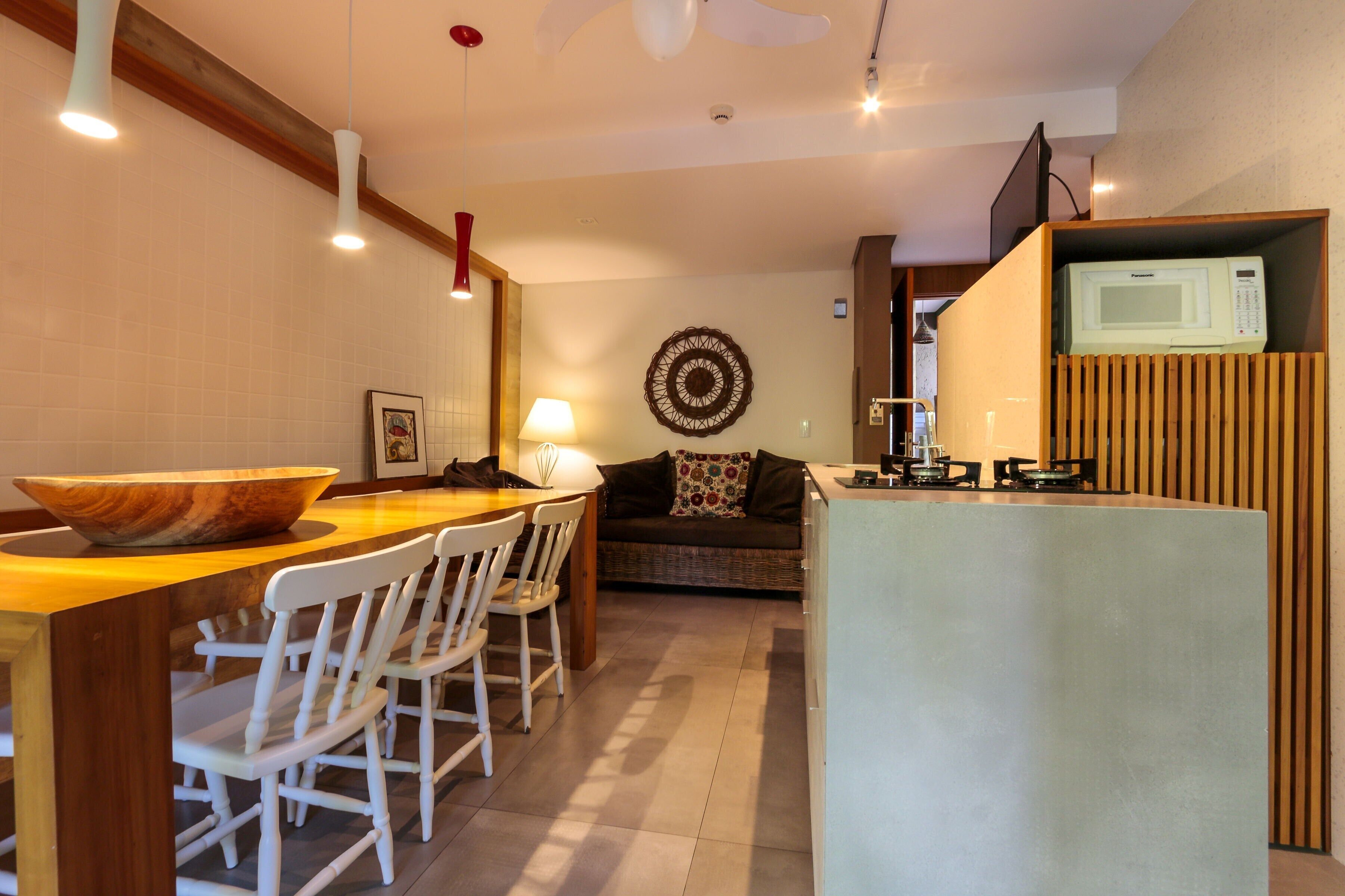 Una cocina moderna con una isla de madera, sillas blancas, una mesa de comedor y un microondas sobre un mueble empotrado.