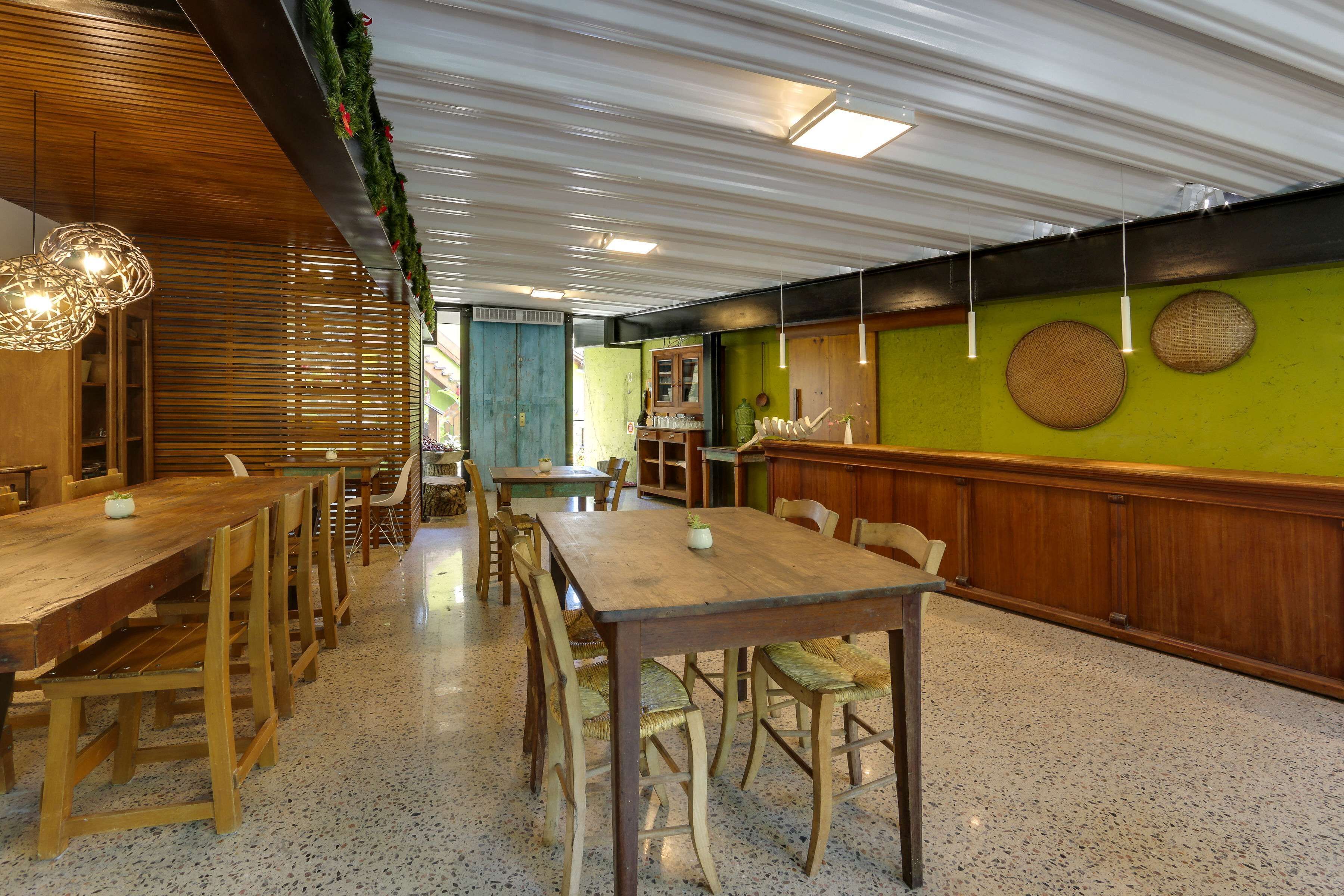 A restaurant with wooden tables and chairs, a green wall, and a ceiling with hanging lights.