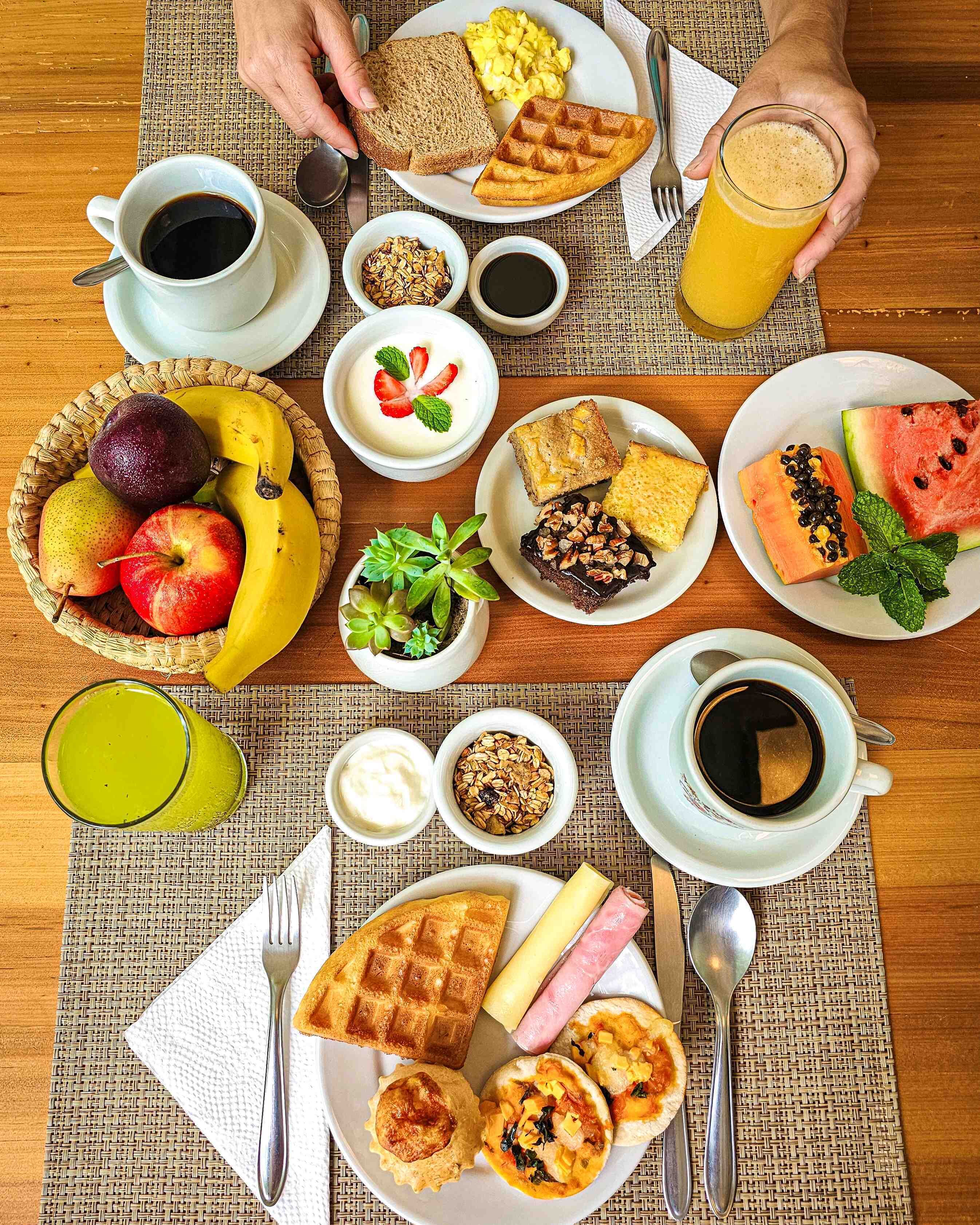 A breakfast spread with toast, waffles, scrambled eggs, and various fruits and pastries.