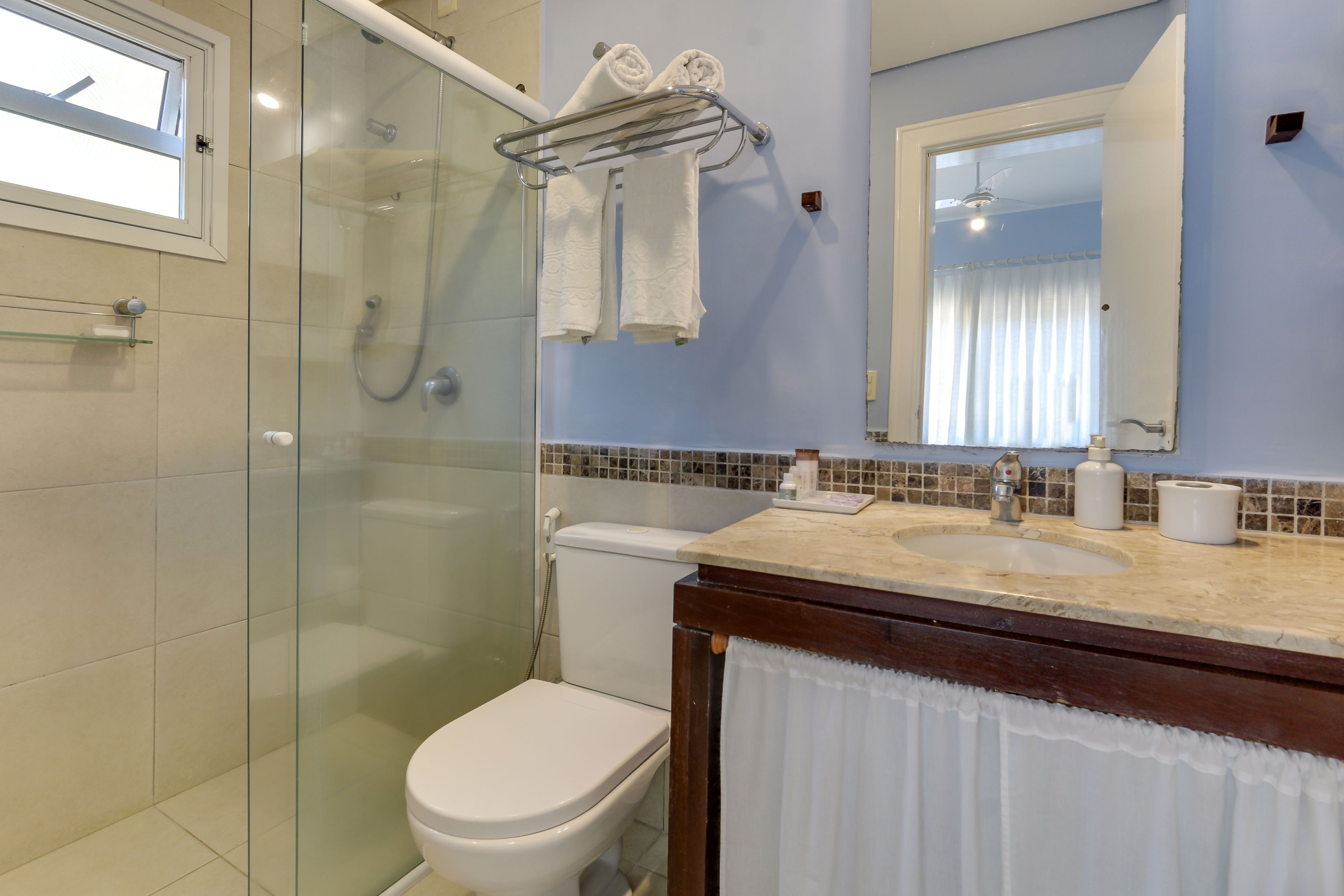 Un baño con ducha envuelta en vidrio, inodoro, lavabo con espejo y toallero con toallas.