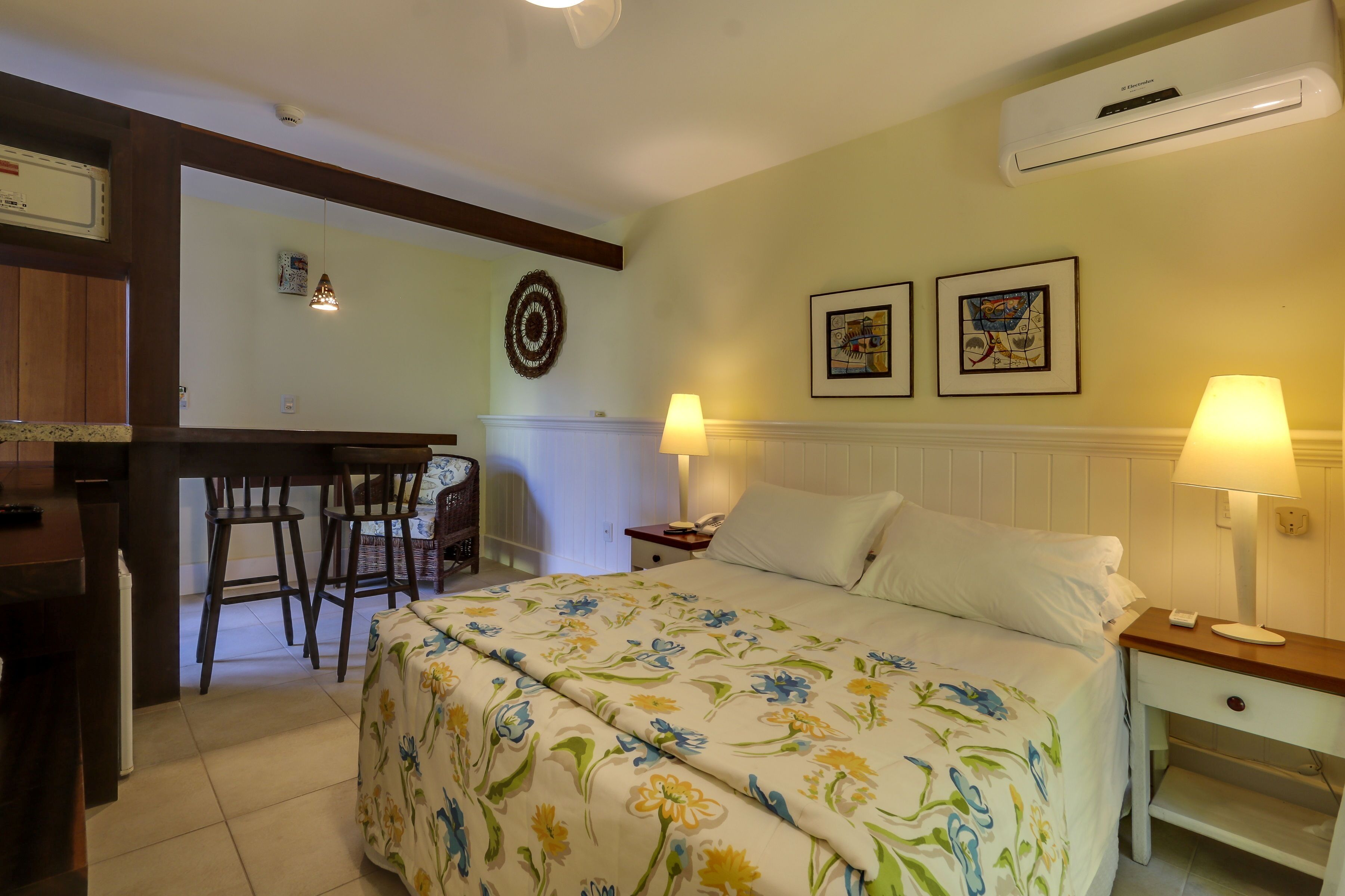 Une chambre d’hôtel comprenant un lit, deux lampes de chevet, une table de chevet, un bureau avec une chaise et un climatiseur fixé au mur.