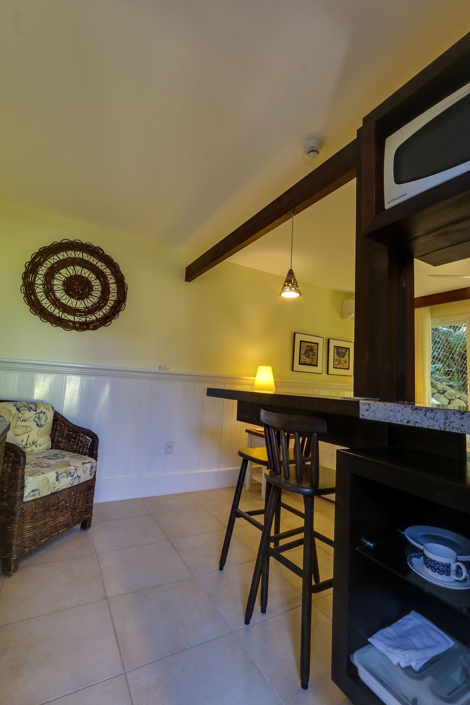 A cozy dining area with a wicker chair, a wooden table, and a hanging pendant light.