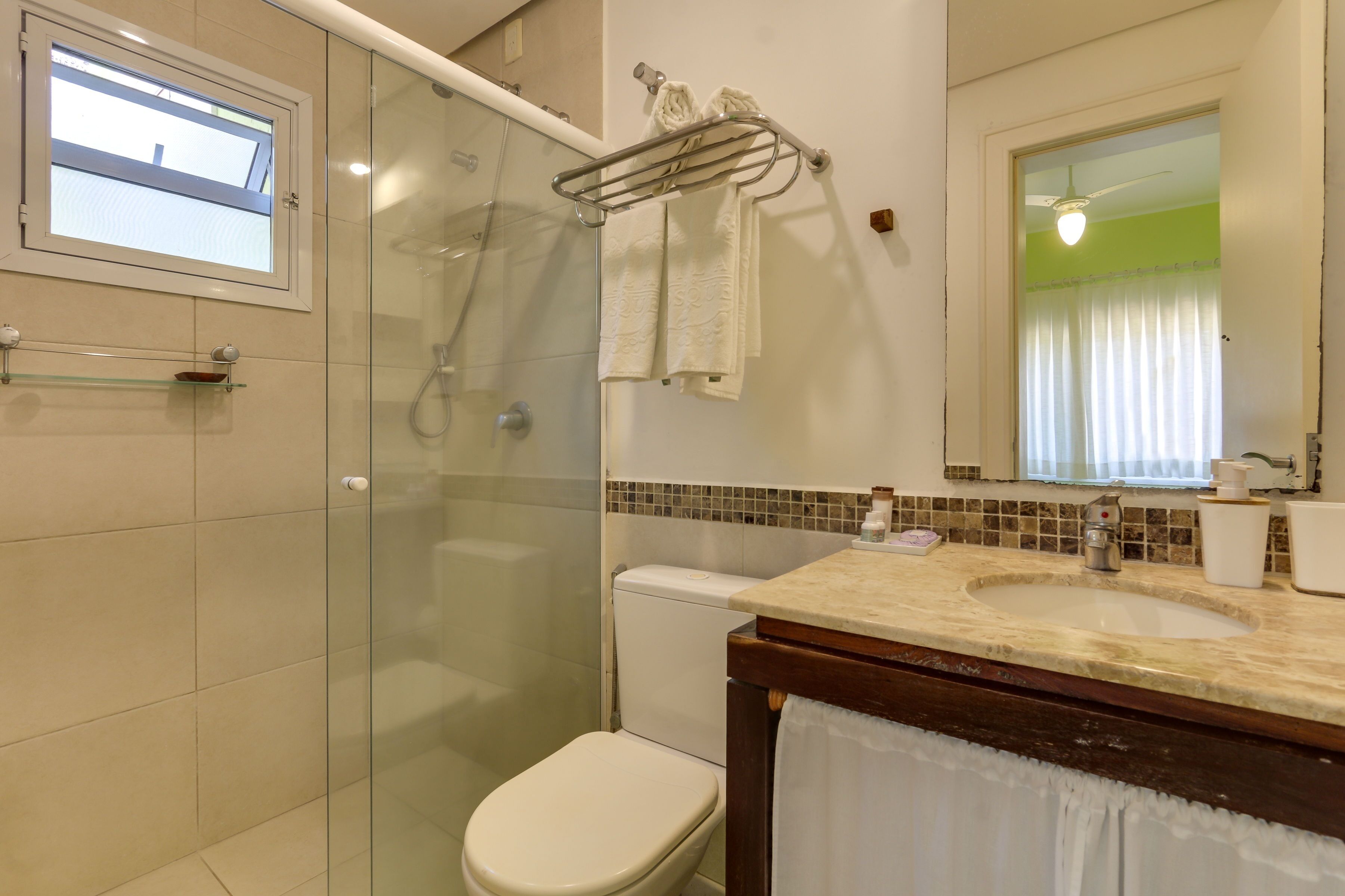 A bathroom with a glass shower enclosure, a toilet, a sink with a mirror, and a window with a view.