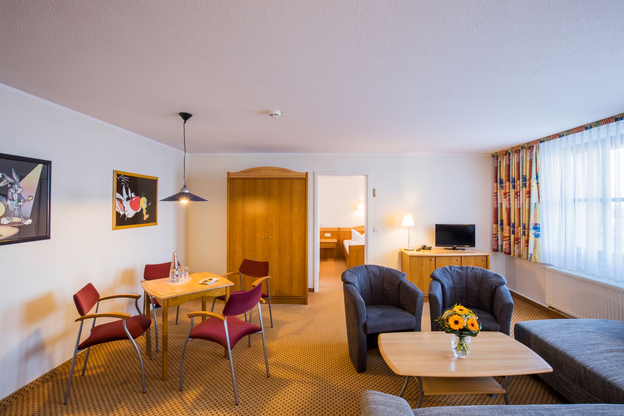 Habitación de hotel con comedor, sofá, televisor y ventana con cortinas.