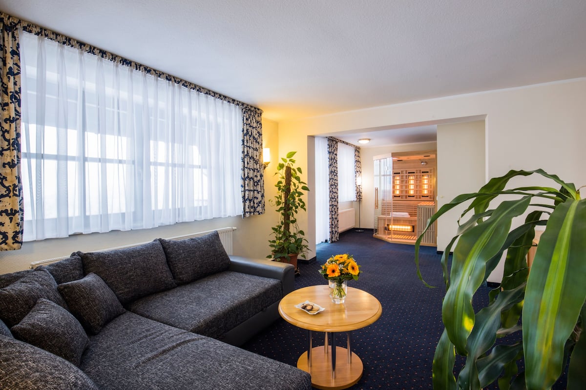 A modern living room with a grey sofa, a round wooden coffee table with a vase of flowers, and a large potted plant.