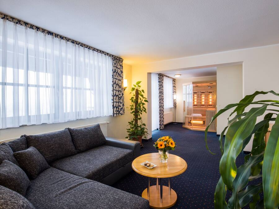 A modern living room with a grey sofa, a round wooden coffee table with a vase of flowers, and a large potted plant.