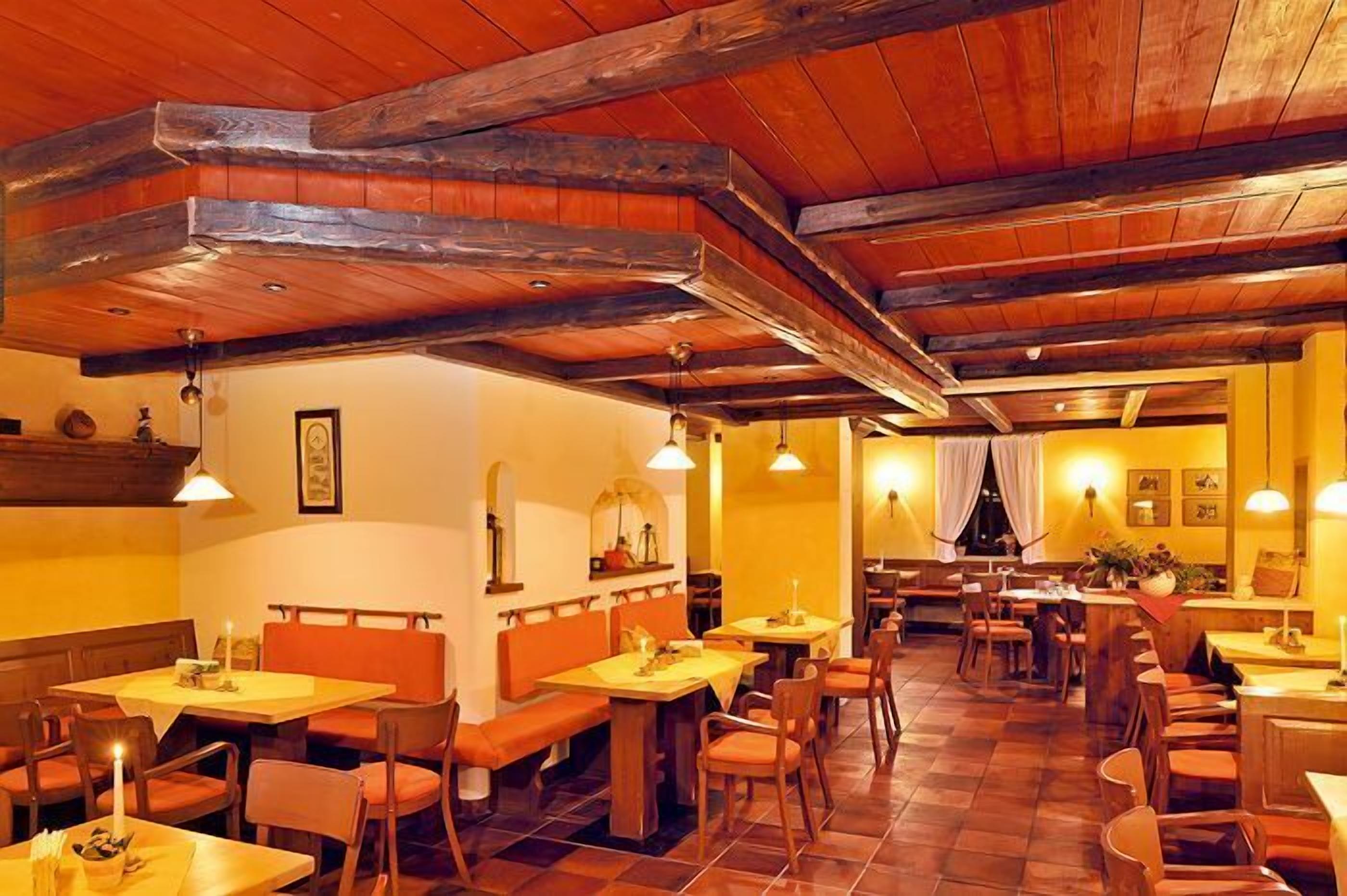 Ein Restaurant mit Holzbalken, orangefarbenen Sitzecken und Tischen mit Kerzen.