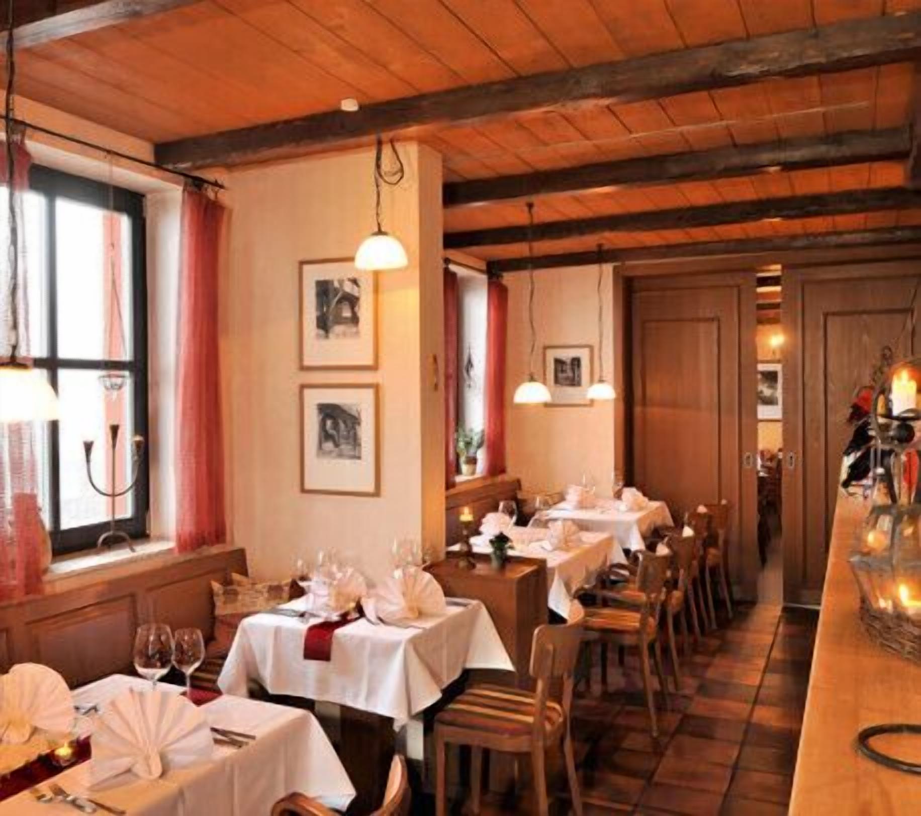 A restaurant with wooden beams, white tablecloths, and framed pictures on the walls.