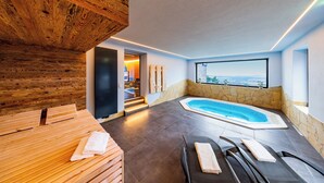 Un área de spa moderna con techo de madera, pared de piedra, bañera de hidromasaje y vistas a la ciudad.