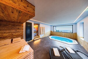 Un área de spa moderna con techo de madera, pared de piedra, bañera de hidromasaje y vistas a la ciudad.