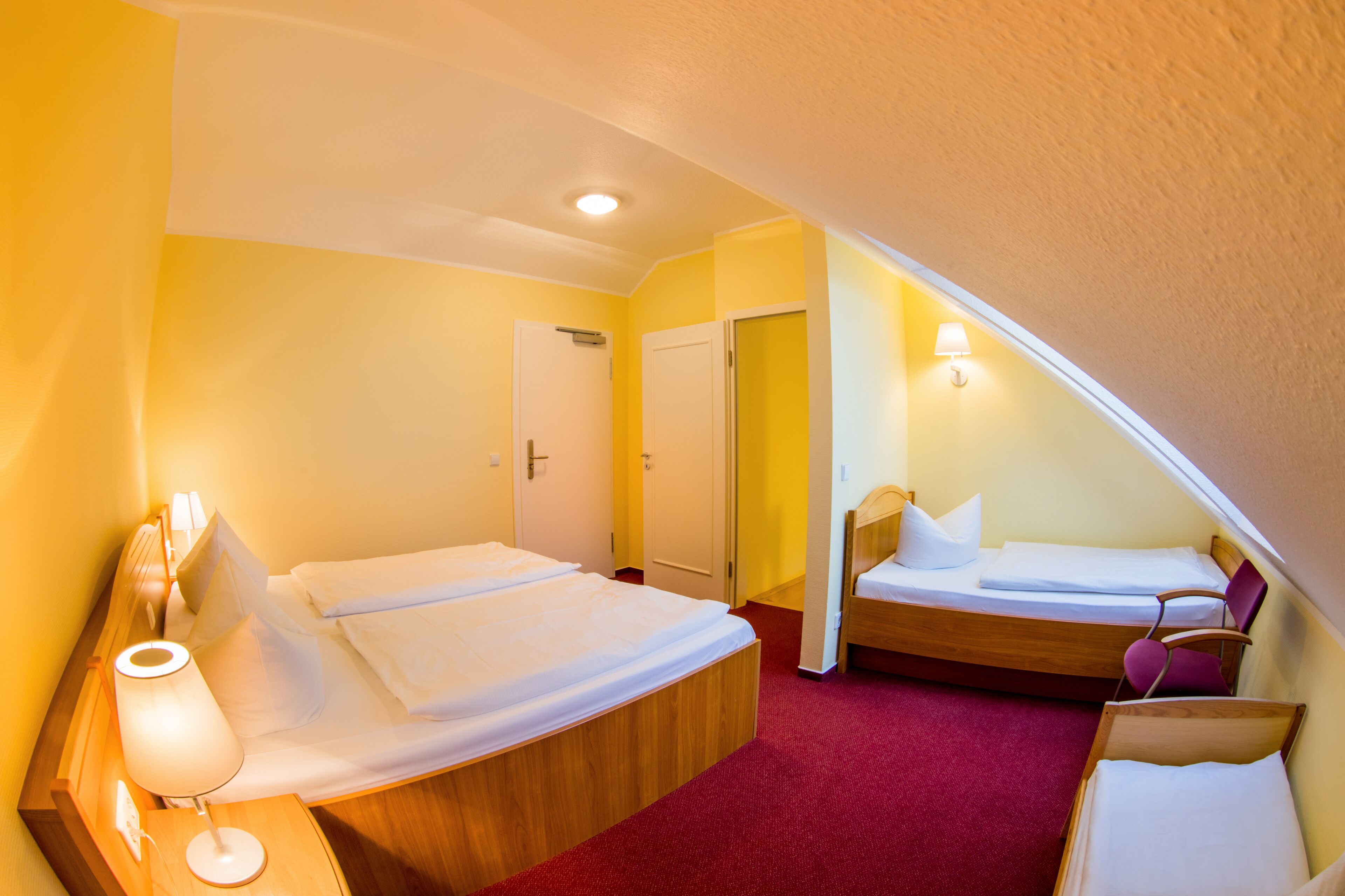 A hotel room with two beds, a red carpet, and a ceiling light.
