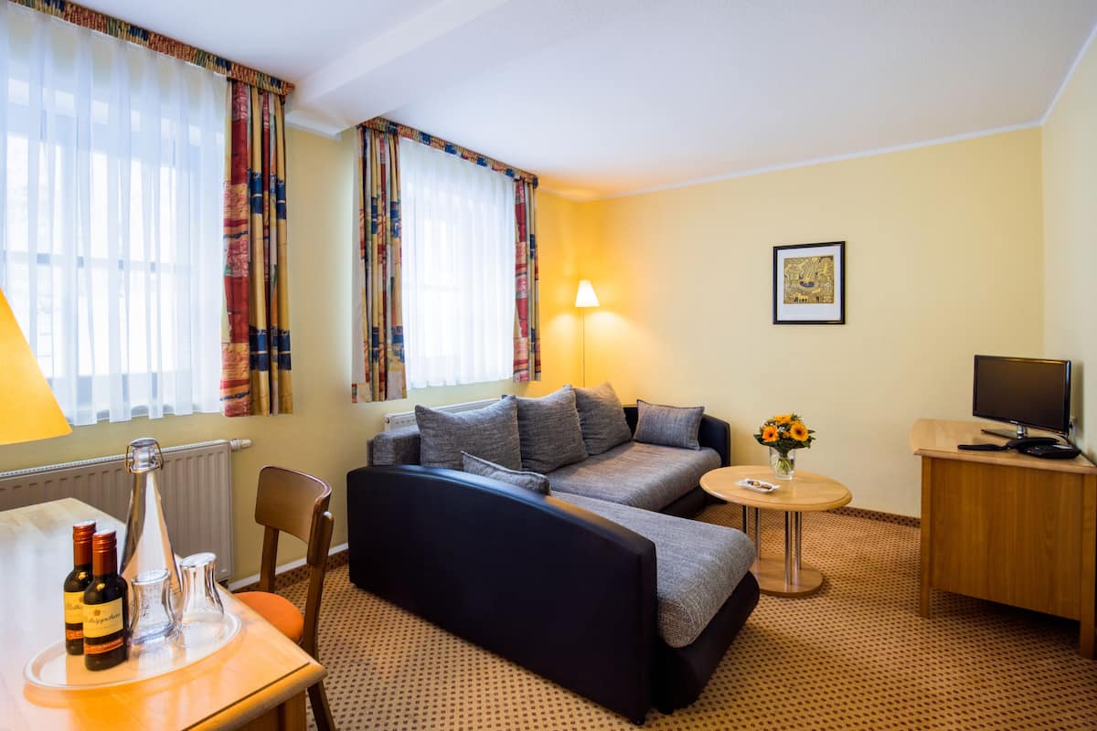 A hotel room with a sofa bed, a small table with a lamp, a TV, and a picture on the wall.