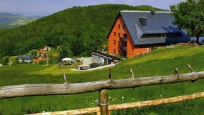Un paisaje rural con una construcción destacada de techo rojo, rodeada de exuberantes campos verdes y una colina boscosa.