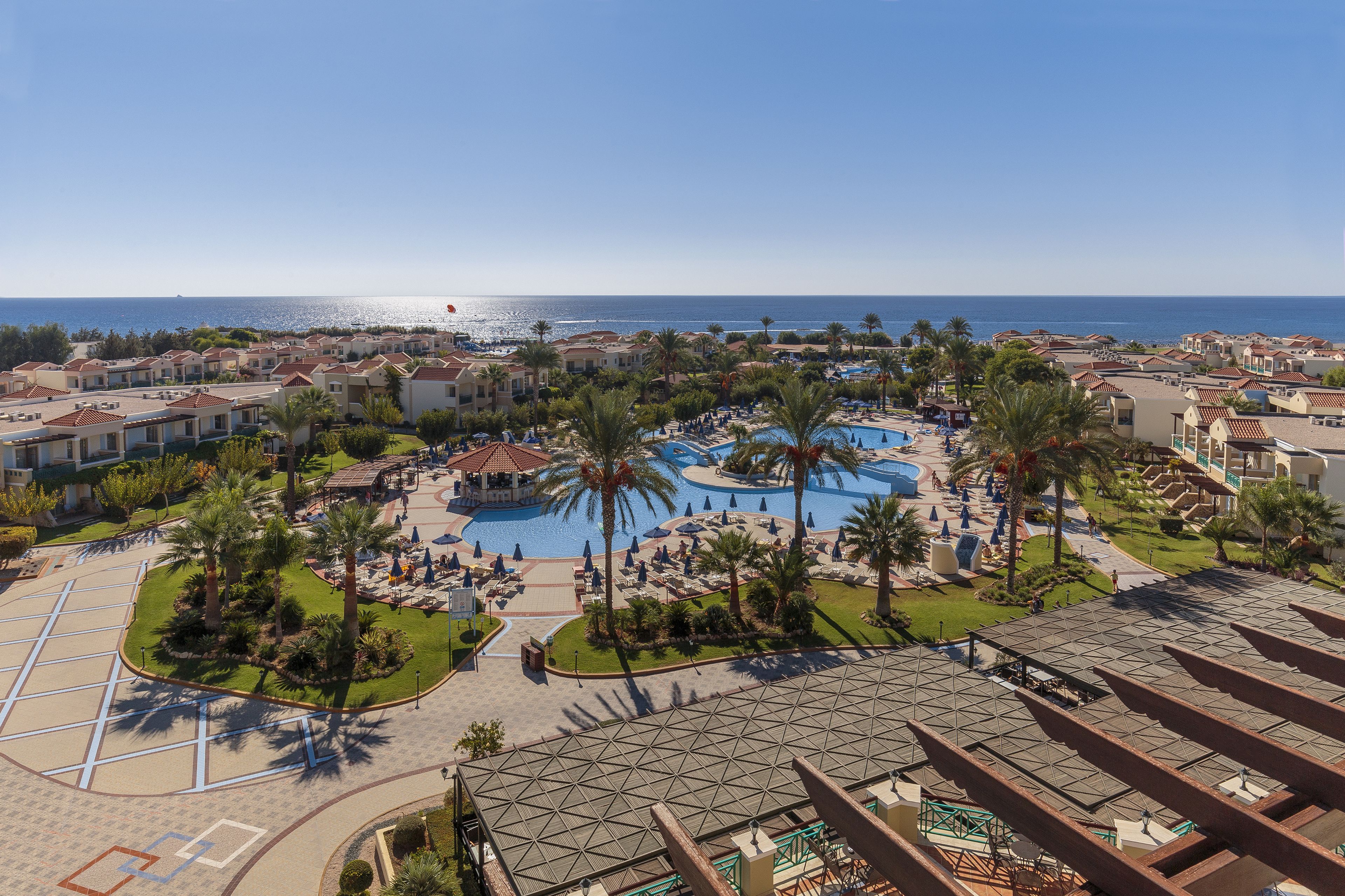 Un resort con piscina central, palmeras y vistas al mar.