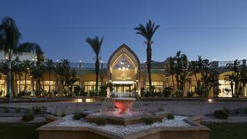 A hotel with a fountain in the courtyard, palm trees, and a well-lit entrance.