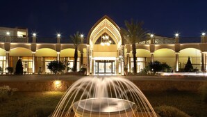 A hotel entrance with a fountain in the foreground, a large arched entrance, and multiple balconies with lighting. - Lindos Princess Beach Hotel All Inclusive (Rhodes)