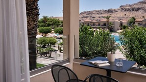 A balcony with a view of a pool, palm trees, and a building complex in the background. - Lindos Princess Beach Hotel All Inclusive (Rhodes)