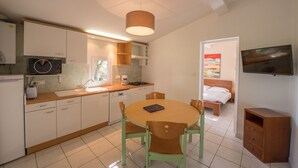 A compact kitchen with a dining area, a TV mounted on the wall, and a bedroom visible through an open door. - Les Hauts de Porto Vecchio (Porto-Vecchio)
