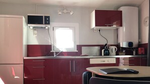 A compact kitchen with red cabinets, a microwave, a coffee maker, and a small dining table. - Les Hauts de Porto Vecchio (Porto-Vecchio)