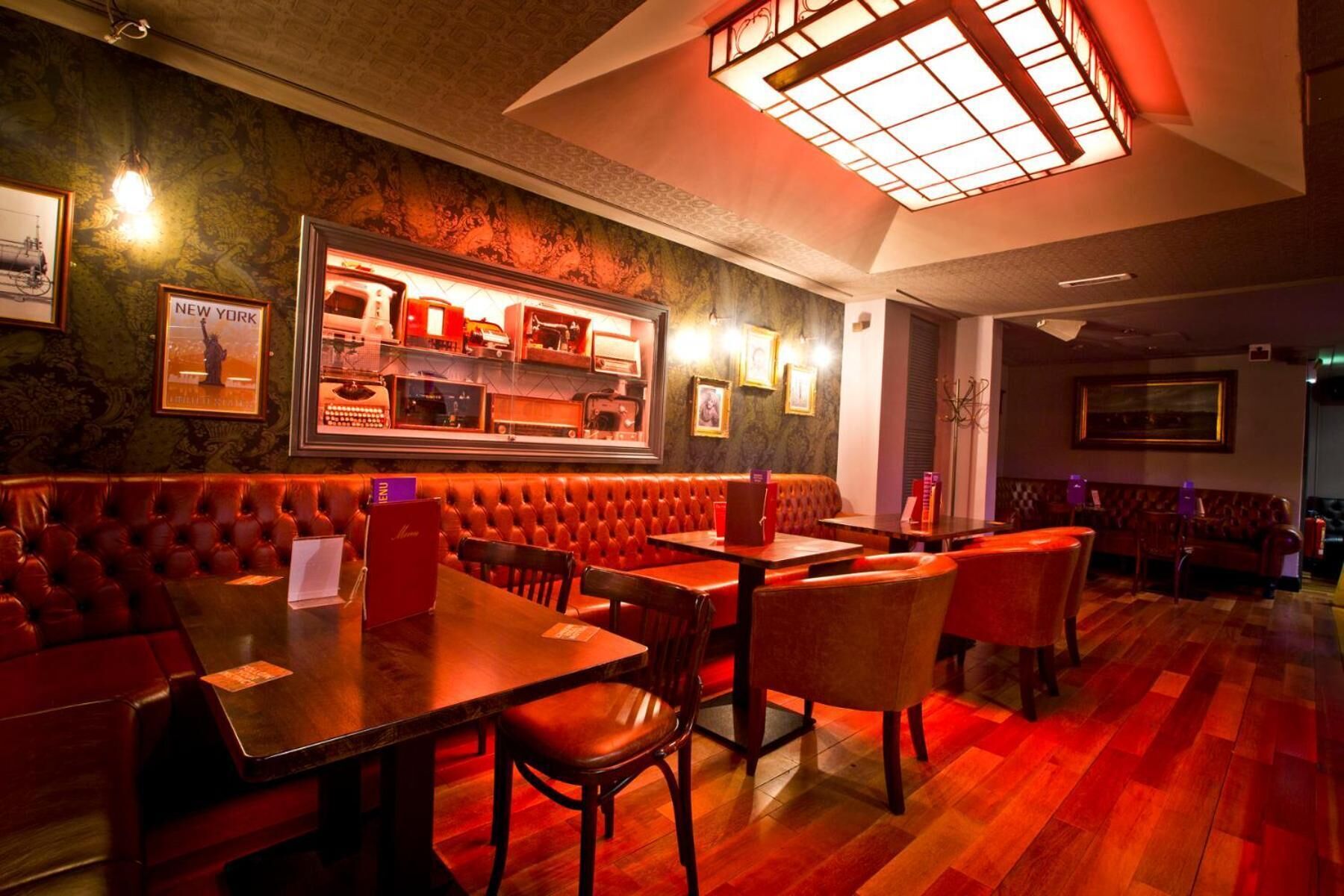 Un restaurante con asientos de cuero rojo, mesas de madera y una zona de bar con objetos antiguos.