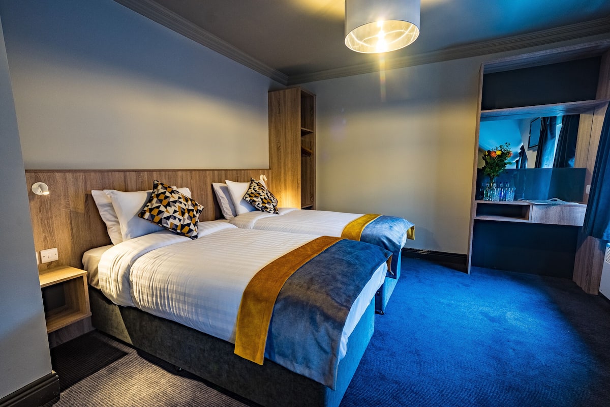 A hotel room with a large bed, a wooden headboard, a nightstand, a mirror, and a blue carpet.