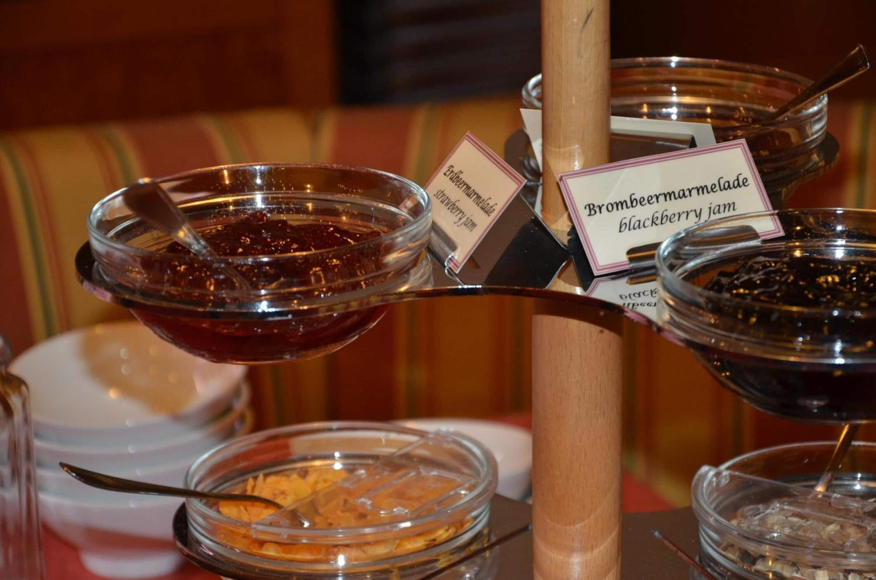 A display of various jams and spreads, including strawberry and blackberry, in clear glass containers with labels.