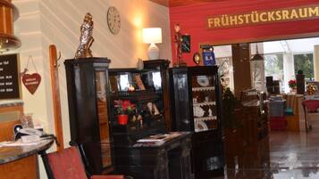 A reception area with a wooden desk, a red chair, a clock, and a sign reading "FRÜHSTÜCKSAUM".