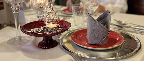 Mesa de jantar posta com pratos vermelhos, talheres e copos, incluindo um castiçal.