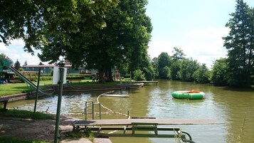 Um parque à beira-rio com um parquinho, uma jangada inflável verde e uma área de água calma.