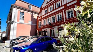 Um hotel com fachada em vermelho e branco, uma torre de sino e uma placa indicando que é um restaurante do hotel.