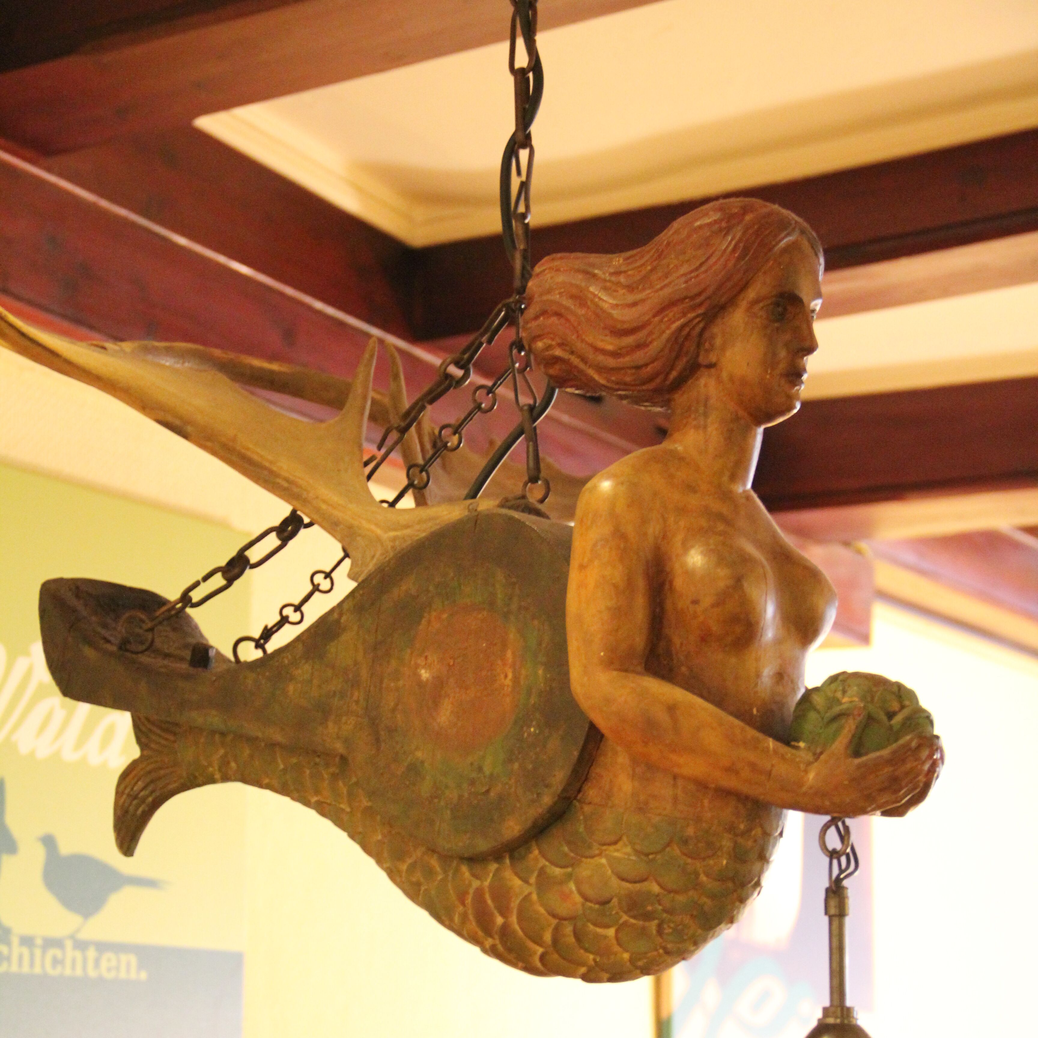 Una escultura de madera de una sirena con cola de pez, colgada del techo.