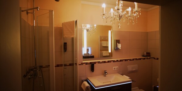 Un baño con cabina de ducha de vidrio, un lavamanos con espejo y una araña.