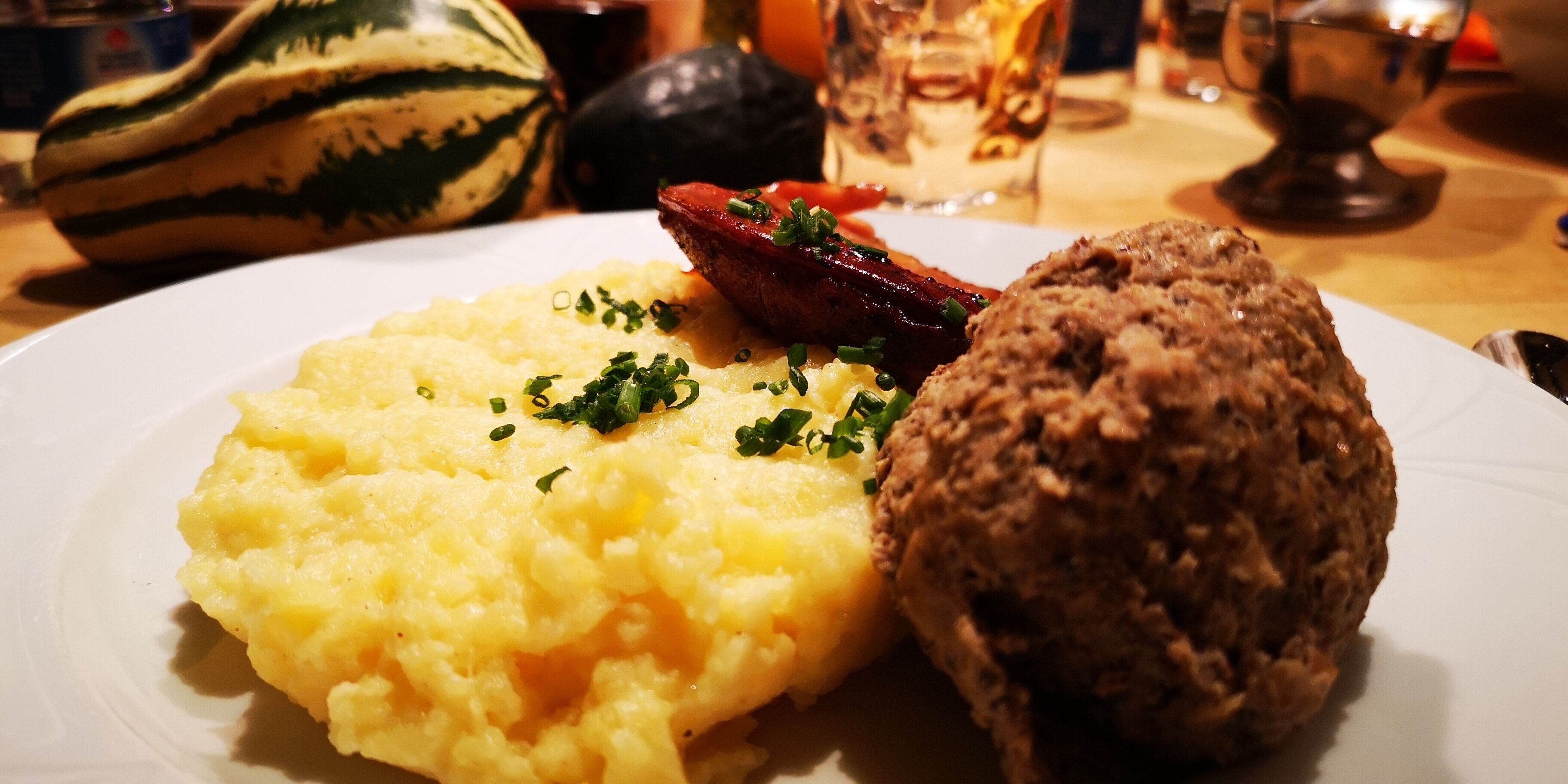 A plate with mashed potatoes, a slice of meat, and a bread roll.