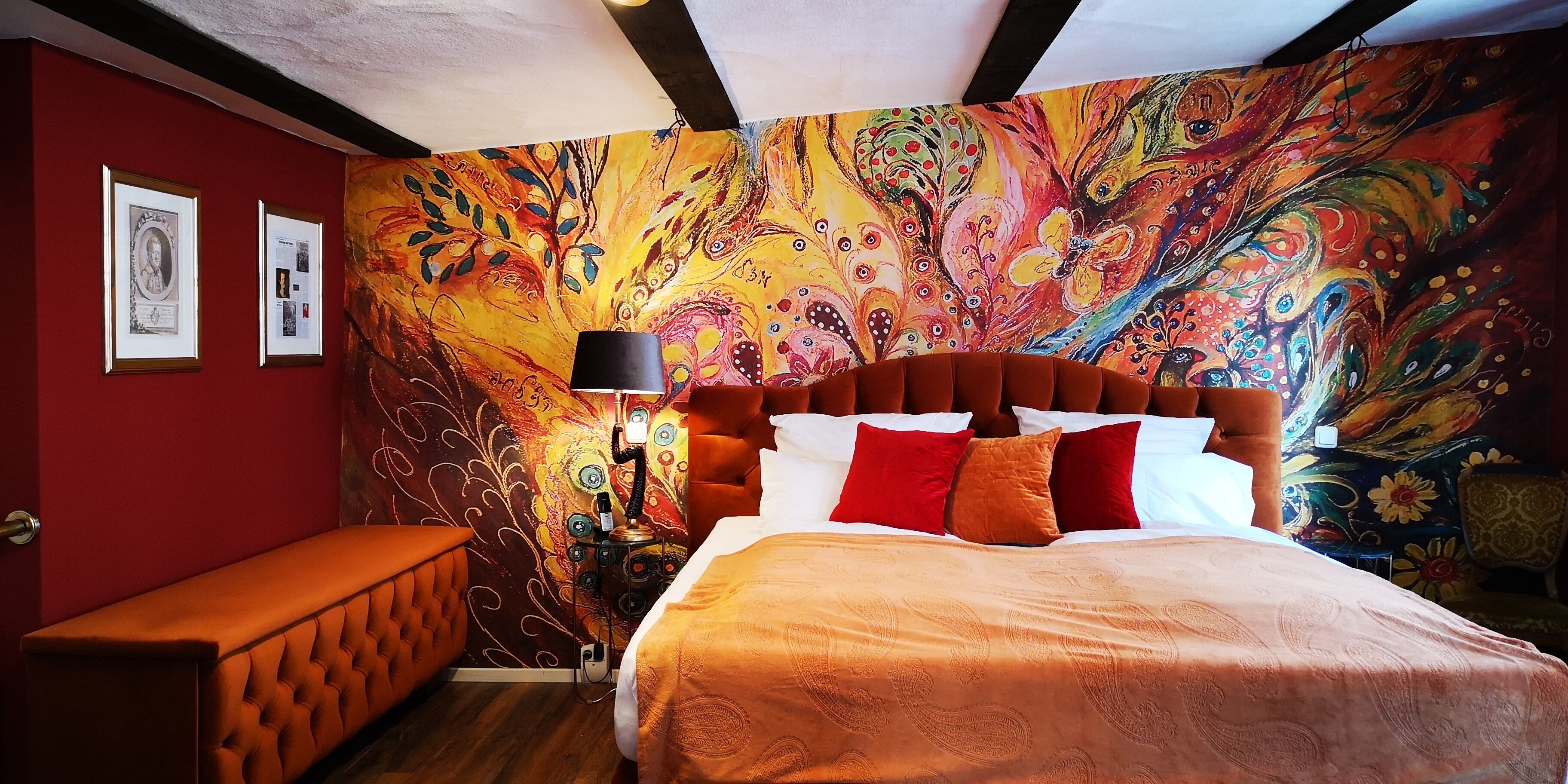 Une chambre à coucher agrémentée d’une fresque murale abstraite aux couleurs vives, d’un banc capitonné et d’un lit avec une literie à motifs.