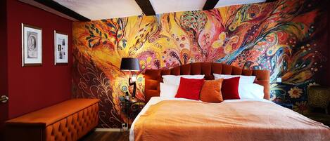Une chambre à coucher agrémentée d’une fresque murale abstraite aux couleurs vives, d’un banc capitonné et d’un lit avec une literie à motifs.