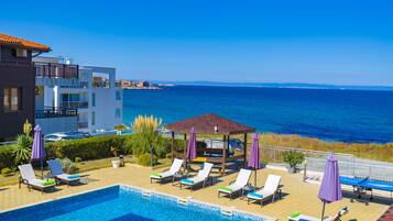 A pool area with lounge chairs and umbrellas, a gazebo, and a view of the sea.