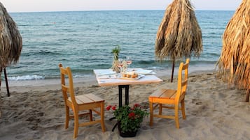 A beachside table with two wooden chairs, a tablecloth, and a potted plant with red flowers.