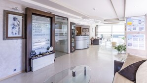 Een moderne hotellobby met een receptiebalie, een glazen salontafel en een zithoek met een bank.