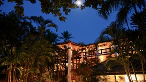 Un edificio de varios pisos, rodeado de palmeras, bajo un cielo nocturno con luna visible.