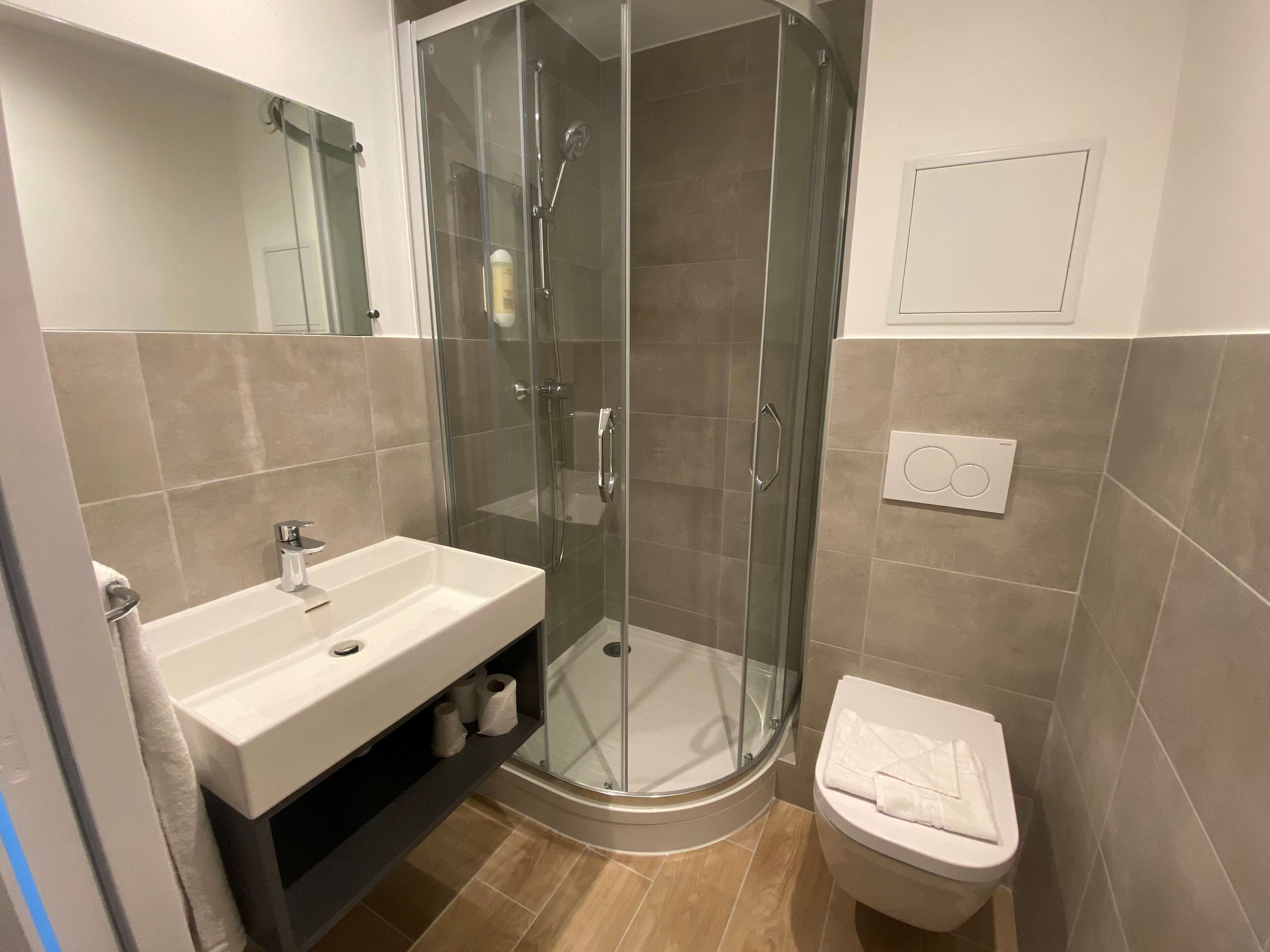 A modern bathroom with a glass-enclosed shower, a white sink, and a toilet.