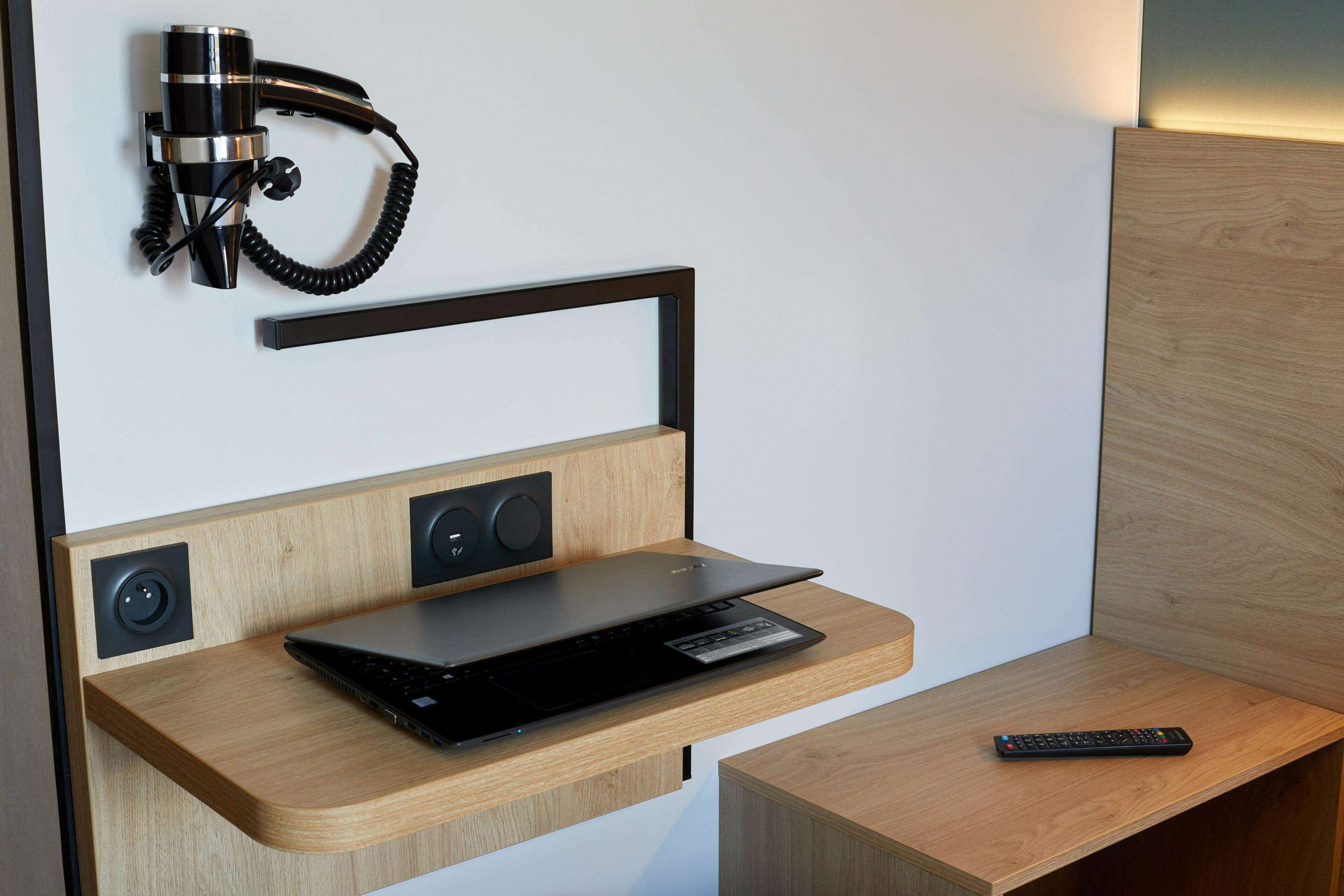 Ein modernes Zimmer mit einem Holztisch, einem Laptop, einer Fernbedienung und einem an der Wand befestigten Telefon.