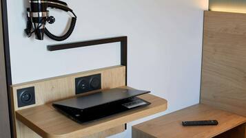 A modern room with a wooden desk, a laptop, a remote control, and a wall-mounted telephone.