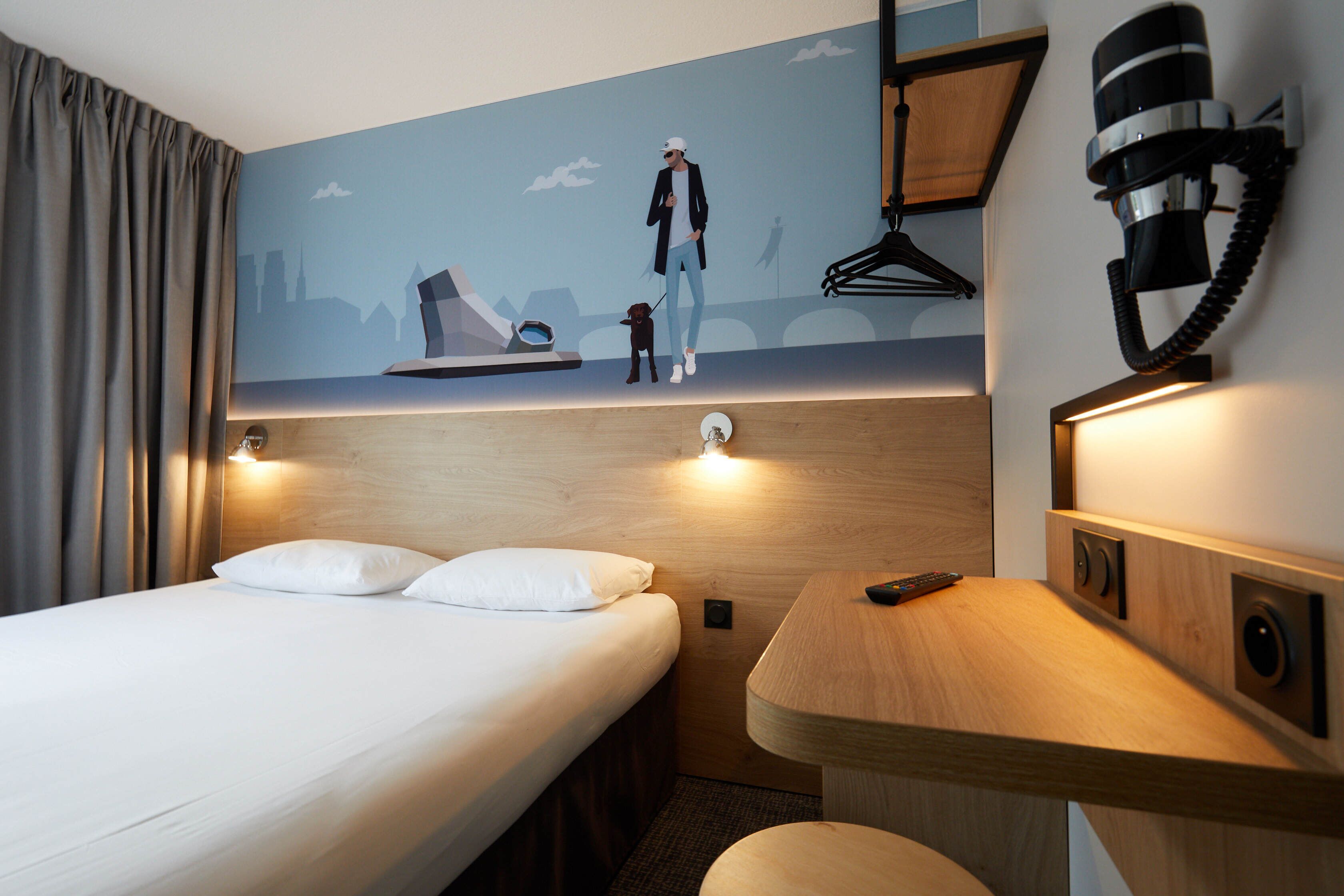 A hotel room with a bed, a desk, and a wall mural.