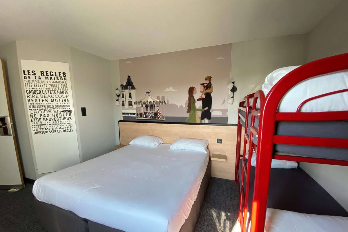 Ein Hotelzimmer mit einem Bett, einem Stockbett, einer Wand mit Wandgemälde und einem Poster mit französischem Text.