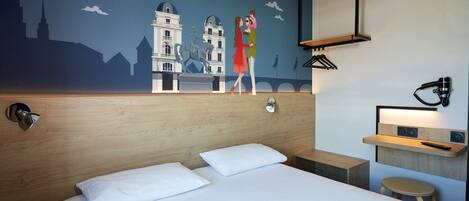 A hotel room with a bed, a nightstand, a wall-mounted shelf, a mirror, and a wall mural depicting a cityscape.