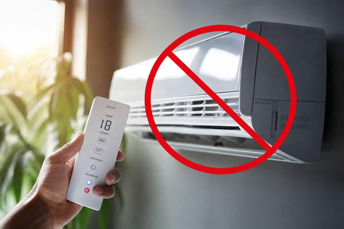 Eine Hand hält eine Fernbedienung vor einer Wand-Klimaanlage, über der ein rotes Verbotsschild angebracht ist.