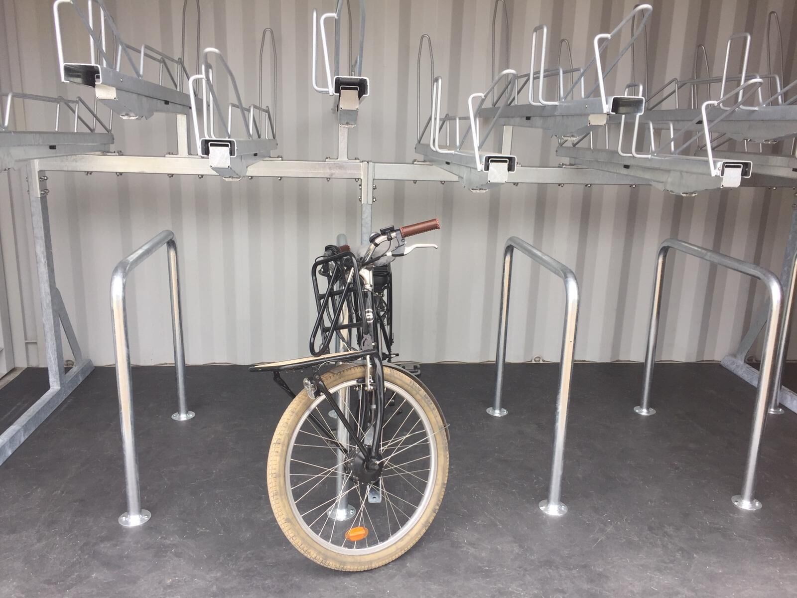 A bicycle secured to a metal rack system in a room with a corrugated metal wall and a concrete floor.