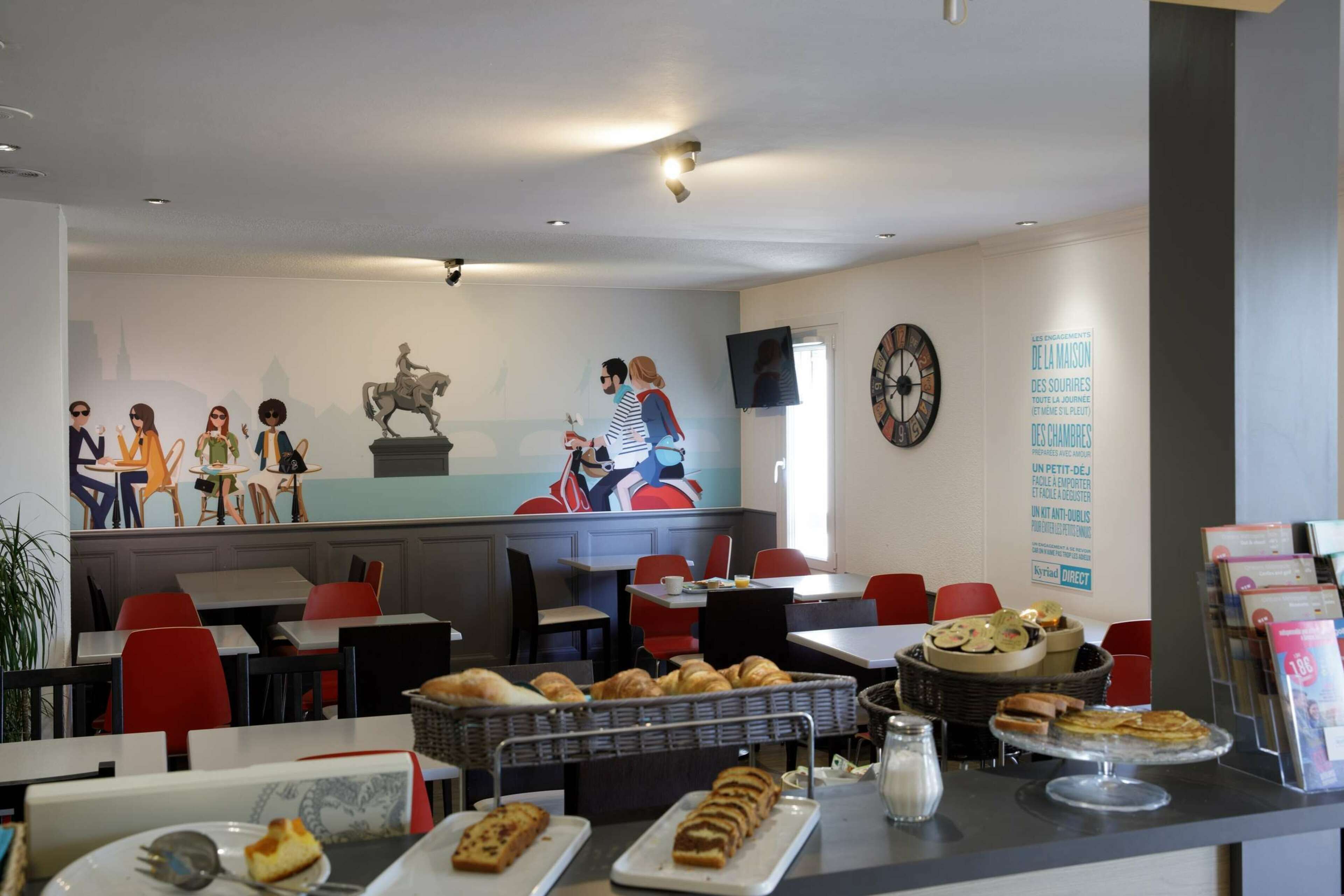 Un restaurant avec des tables et des chaises, un comptoir où sont exposées des pâtisseries, et une fresque murale.
