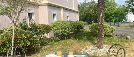 Una mesa con alimentos para el desayuno y una silla frente a un edificio con jardín.